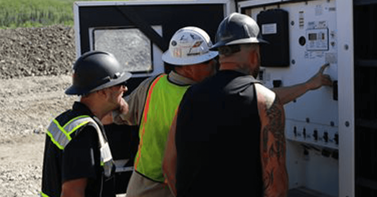 Three workers looking at the inside of a generator in the field.