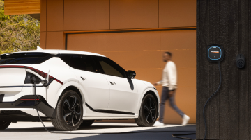 An electric vehicle charging outside a garage while a person walks behind it