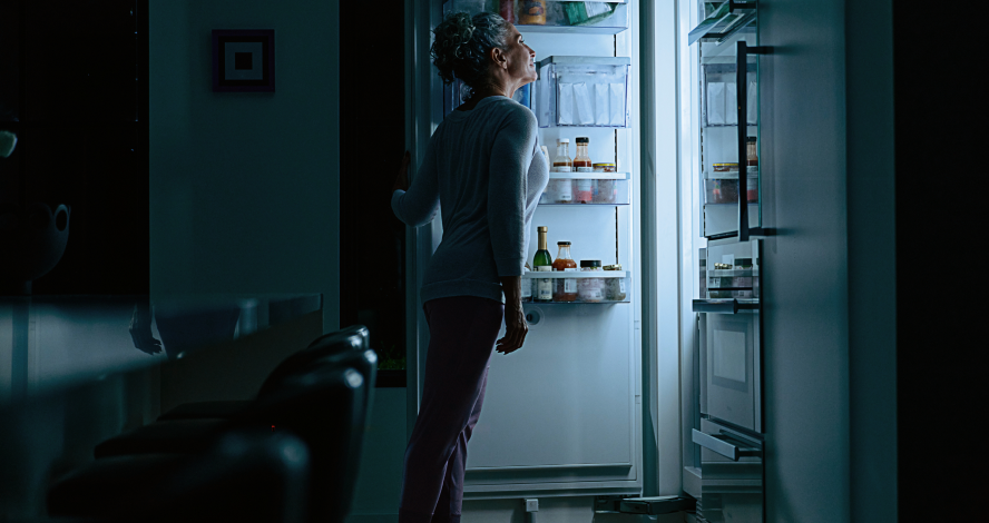 woman peering into bright fridge