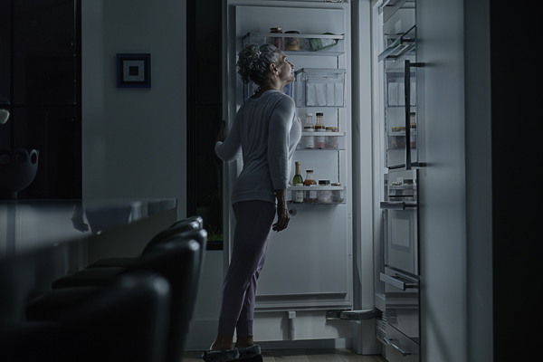 woman in darkness looking through a lit up fridge